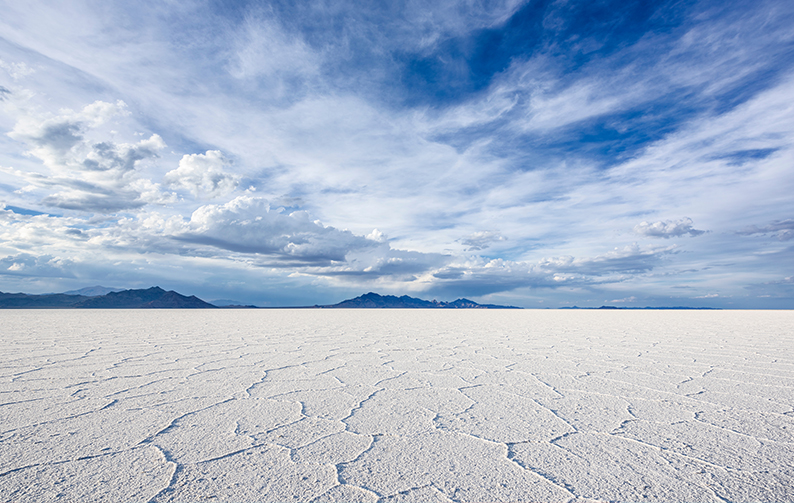 The image shows a large expanse of white salt flats beneath a blue sky with clouds.