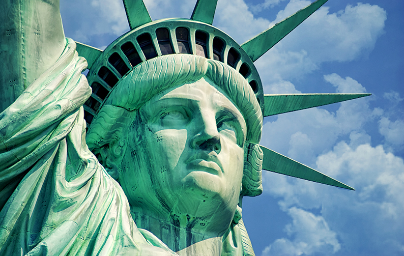 The Statue of Liberty stands tall against a blue sky with puffy white clouds.