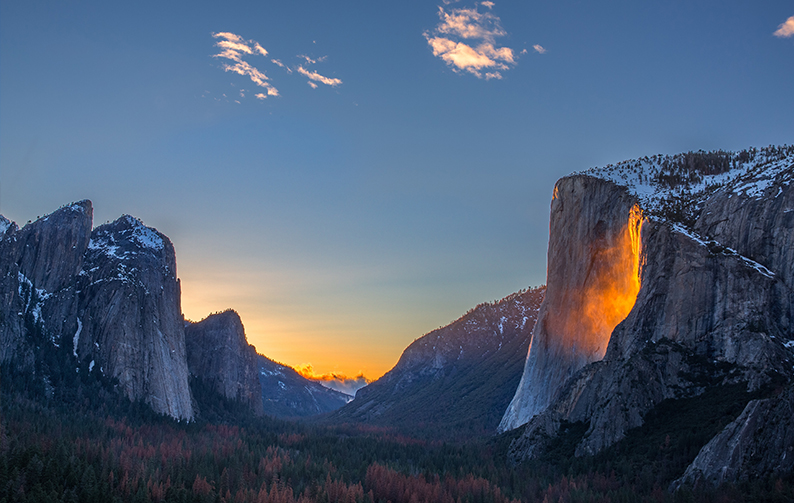 A mountain range with a dramatic cliff face that has a golden glow as the sun sets.