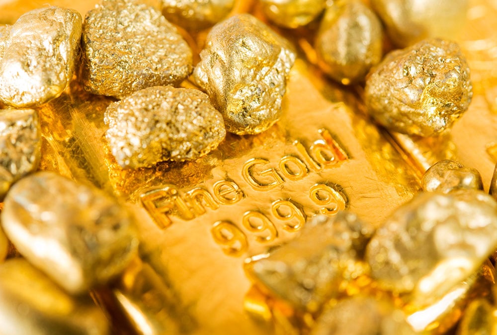 Gold nuggets sit atop a bar of fine gold, stamped "Fine Gold 999.9".