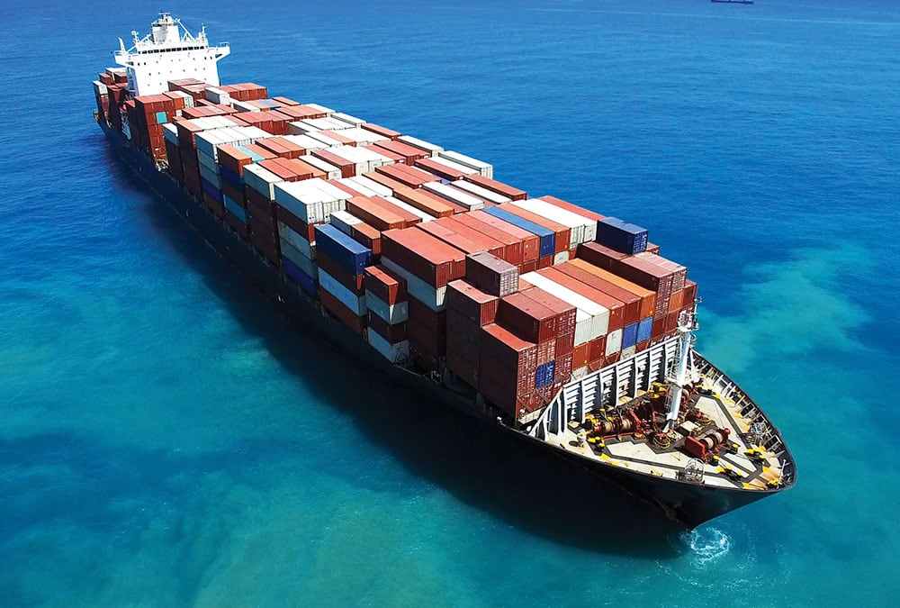 A large cargo ship loaded with containers sails through the ocean.