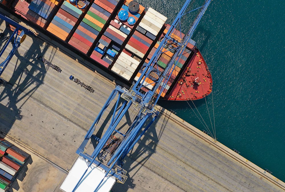 A cargo ship is docked at a port with a crane loading or unloading containers.