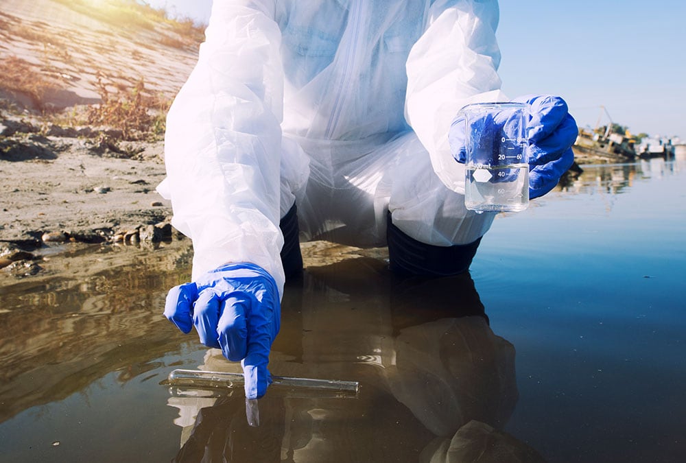 A scientist in protective clothing is testing the water quality of a river or stream.