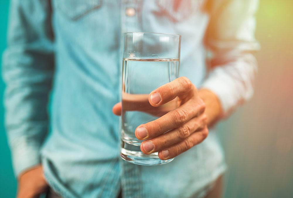 A person holds a glass of water with their hand outstretched.