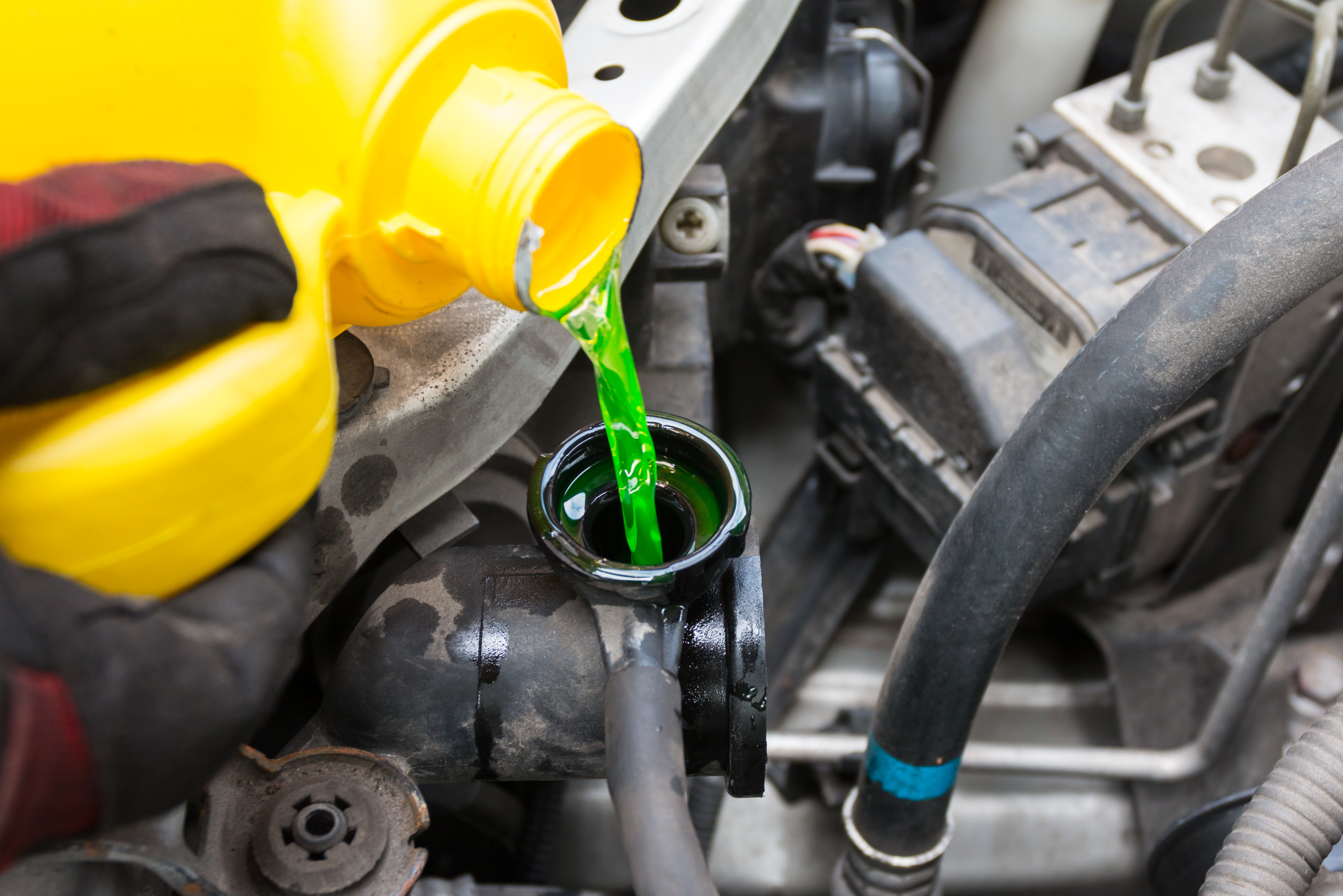 A mechanic pours green coolant into a vehicle's radiator.