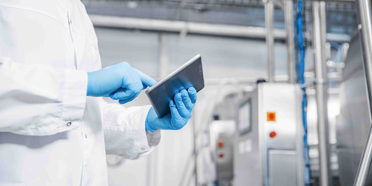 Pessoa com luvas azuis a utilizar um tablet durante uma auditoria numa fábrica.