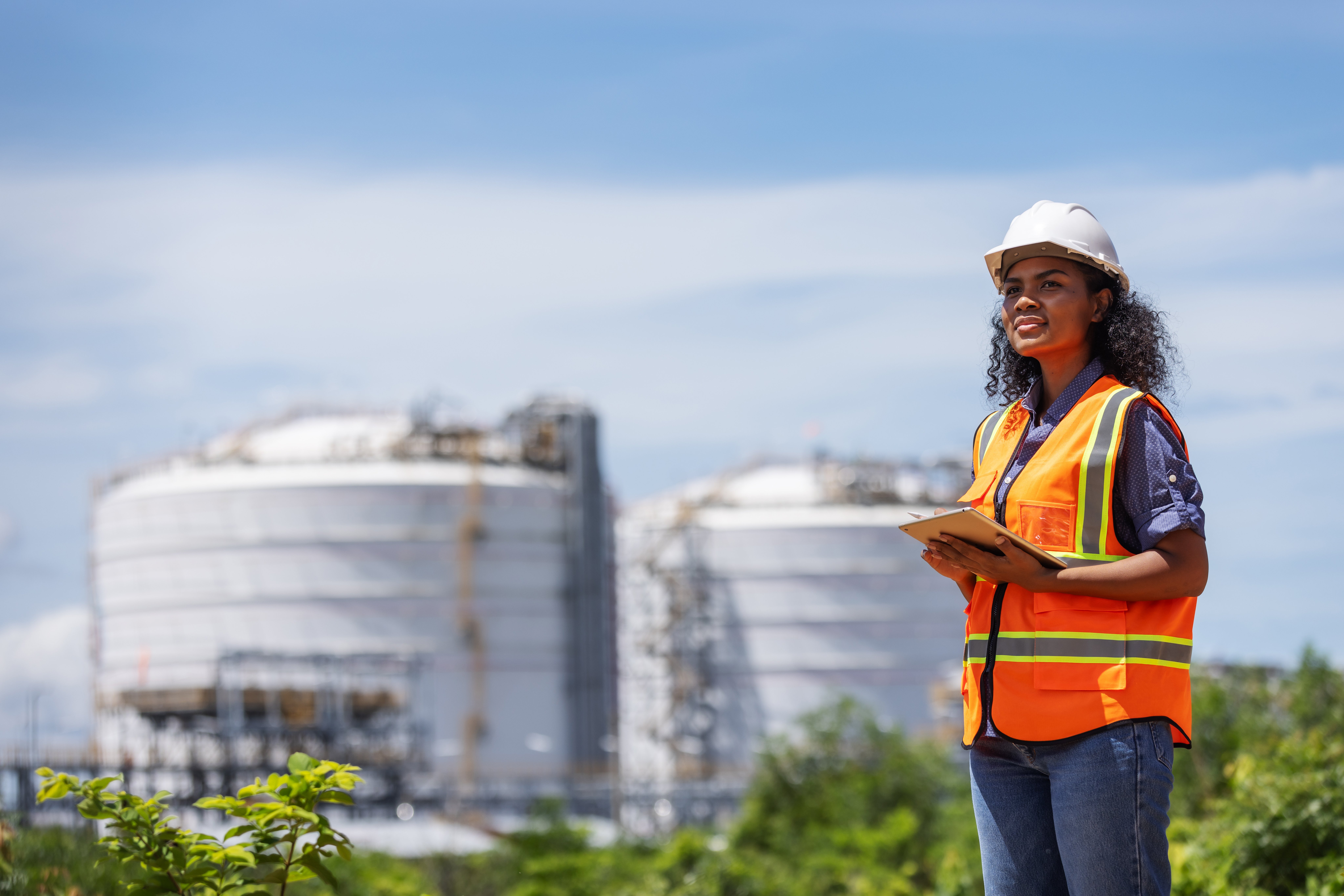 Engineer wearing a helmet and safety vest holding a tablet at an industrial facility.