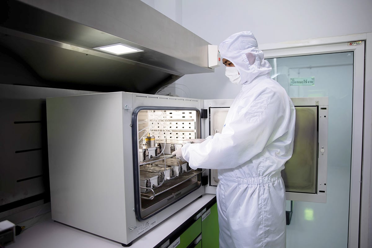 A person wearing cleanroom protective clothing places samples inside an open laboratory thermal desorption or GC‑MS test chamber under a ventilation hood in a controlled laboratory environment.