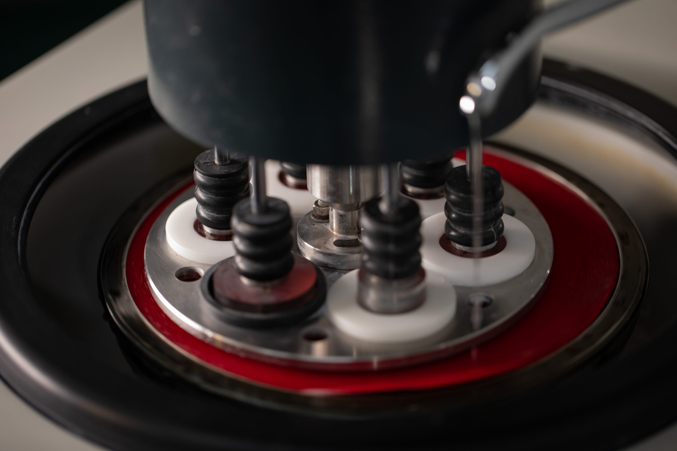 Close‑up view of a micro‑sectioning or polishing machine head pressing multiple sample mounts in a circular holder during laboratory material testing.