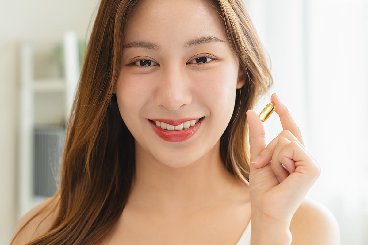 A person holds a single soft‑gel capsule between their fingers against a softly lit indoor background.