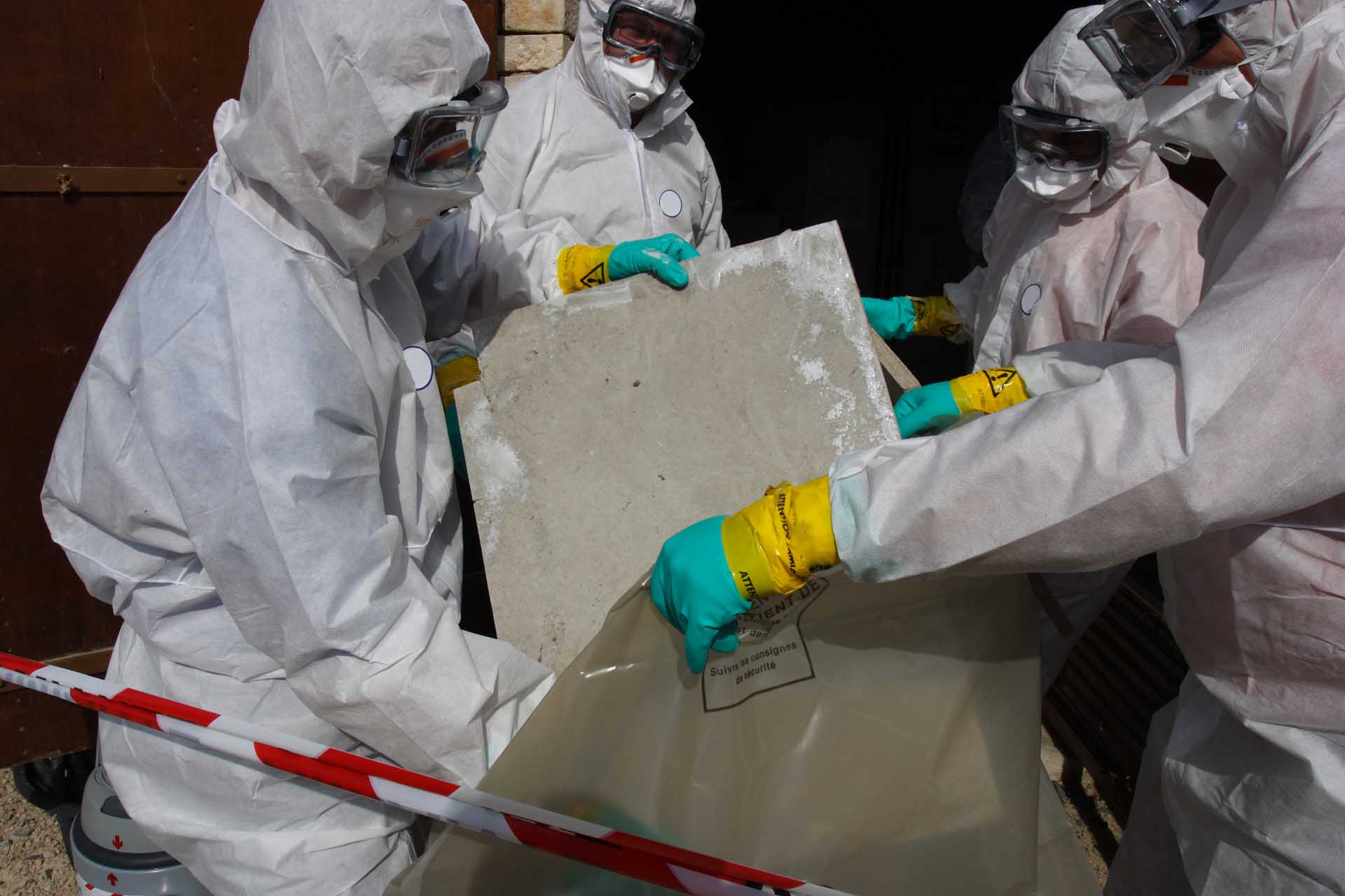Three people are dressed in protective suits while collecting a sample in a plastic bag.