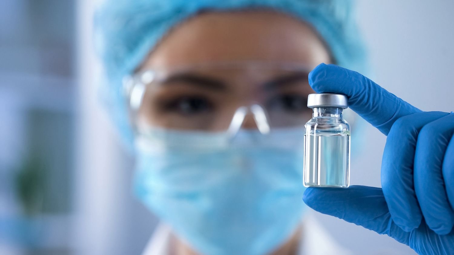 Laboratoriepersonal i skyddsutrustning håller upp ett provrör.