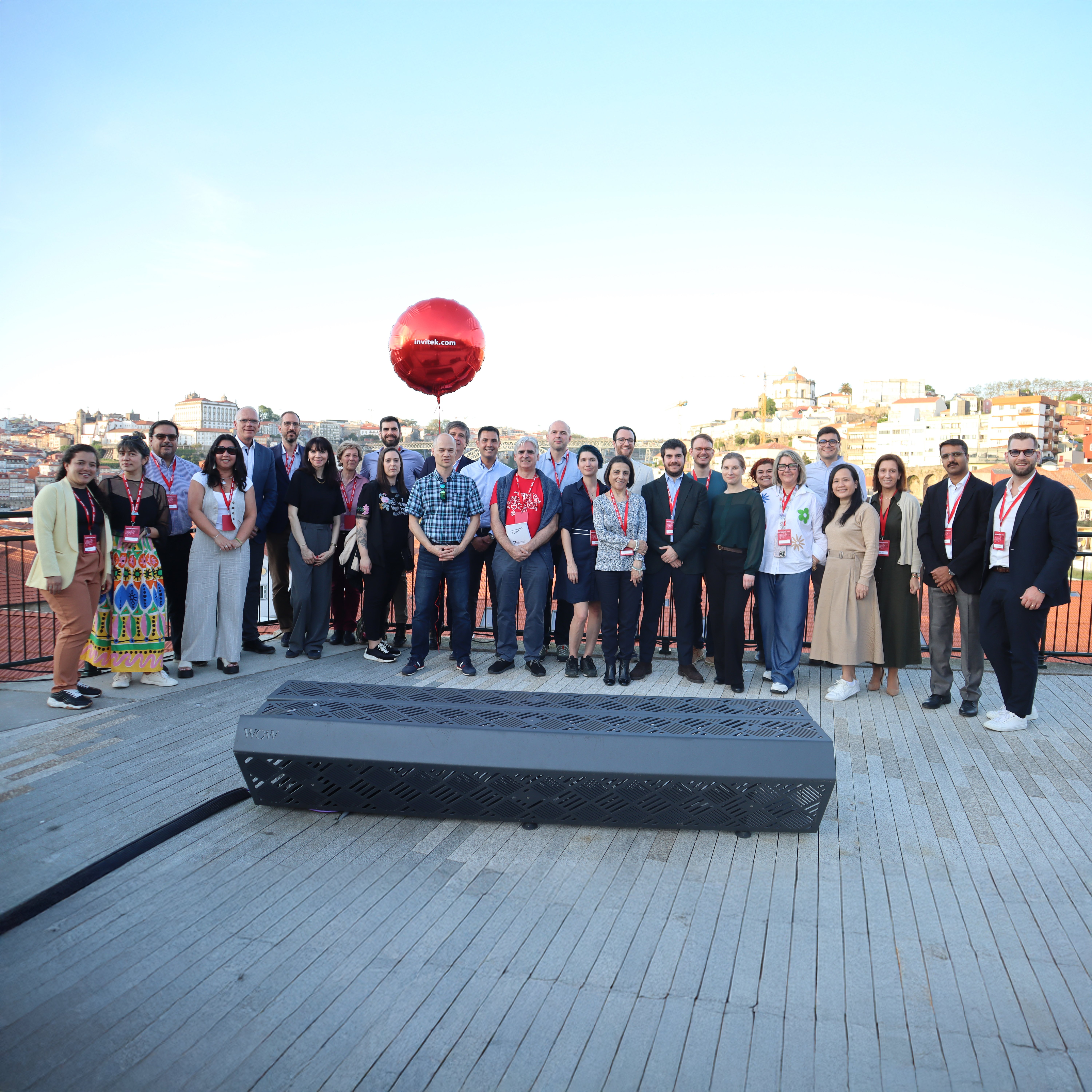 Group of people standing on an outdoor platform with a cityscape in the background and a large red balloon floating above them.