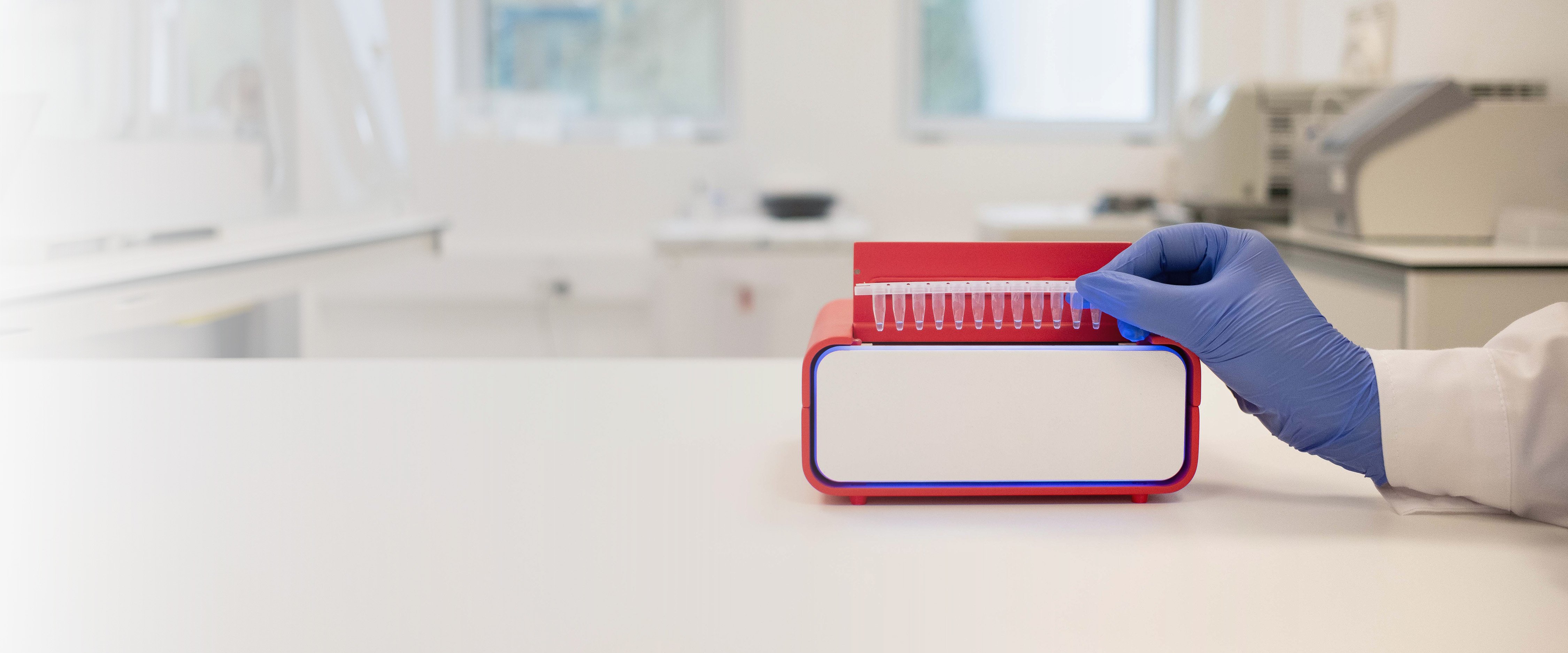 Hand placing a strip of sample tubes onto the InviDx® molecular detection system in a laboratory environment.