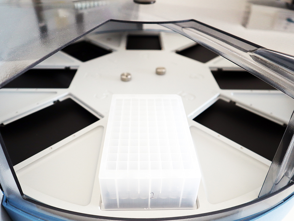 A laboratory centrifuge with an open lid showing a rotor holding a white plastic microplate, used for sample processing.