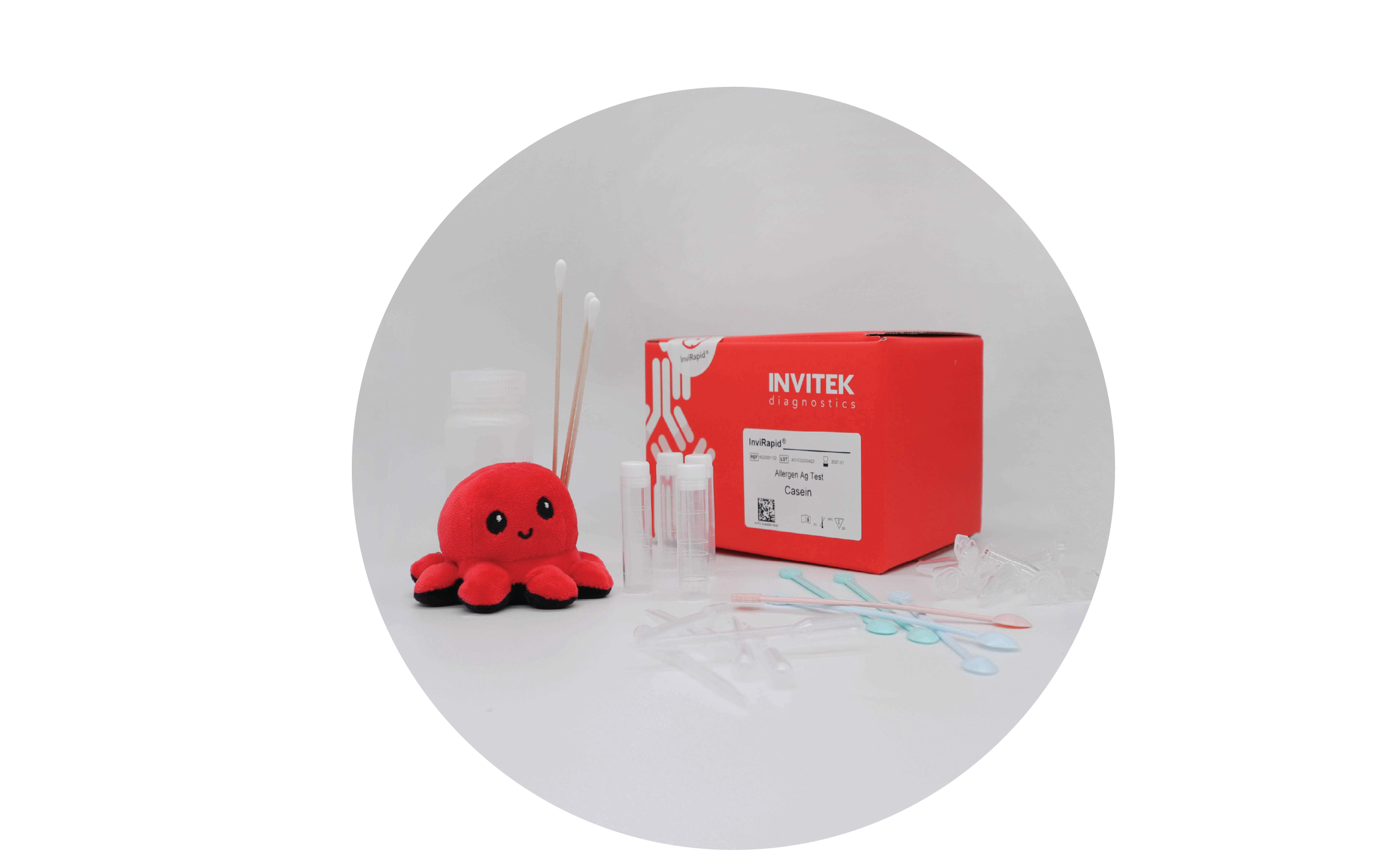Red Invitek Diagnostics InviRapid Casein Allergen Ag Test box behind sample tubes next to swabs and a buffer bottle with scoops, droppers and tubes laying scattered in front.