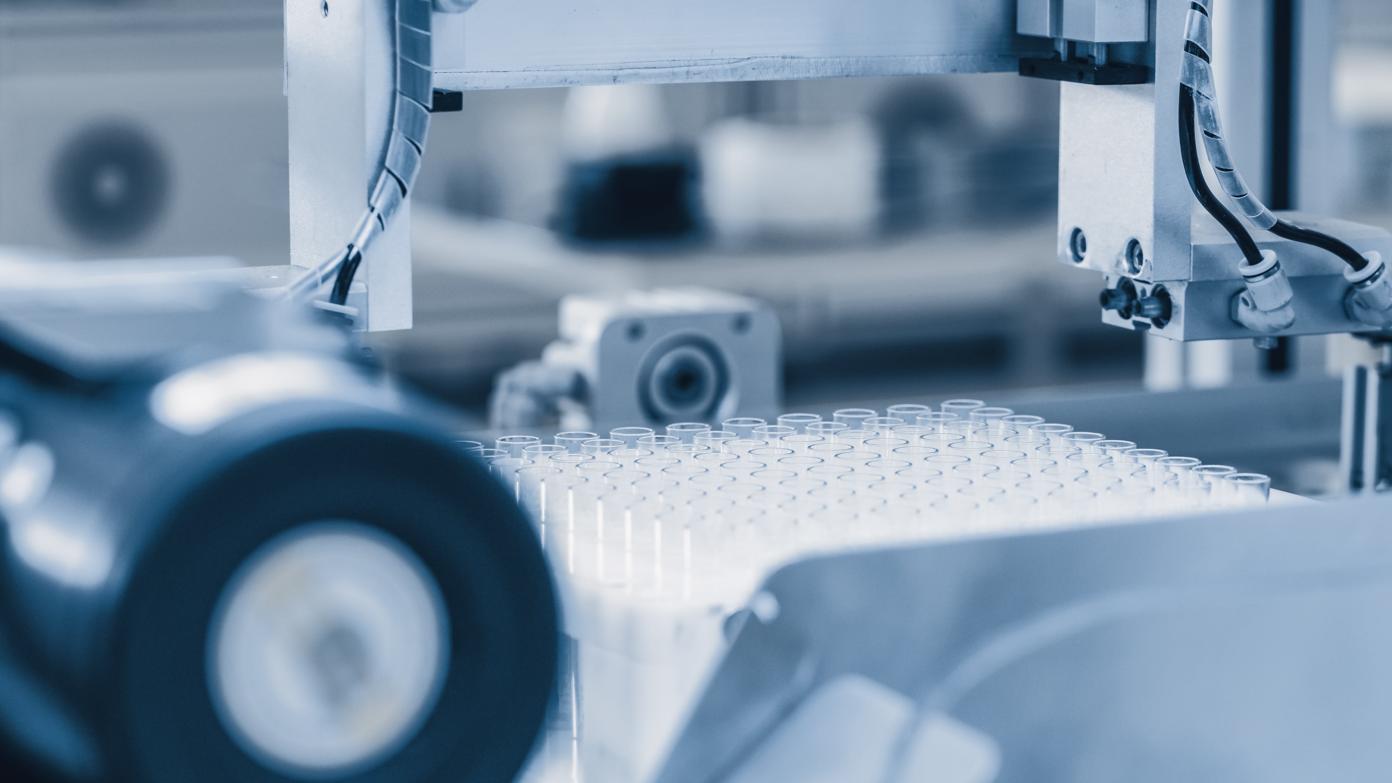 Close-up view of automated laboratory equipment handling a tray of multiple small test tubes, with mechanical arms and precision components visible in a sterile environment