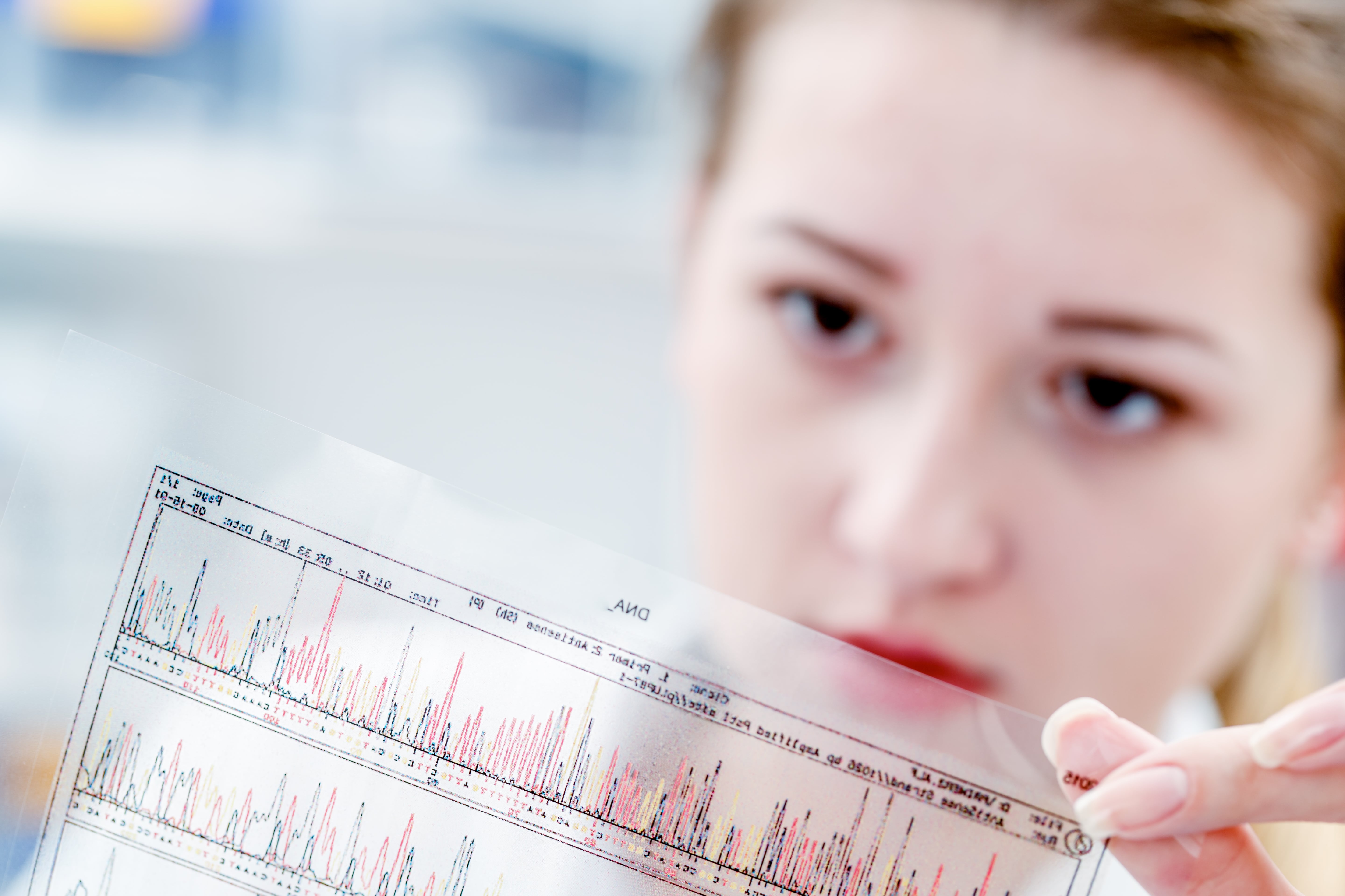 Close-up of a person holding a printed sheet with chromatogram data and colored peaks, typically used for DNA or genetic analysis, in a laboratory setting.