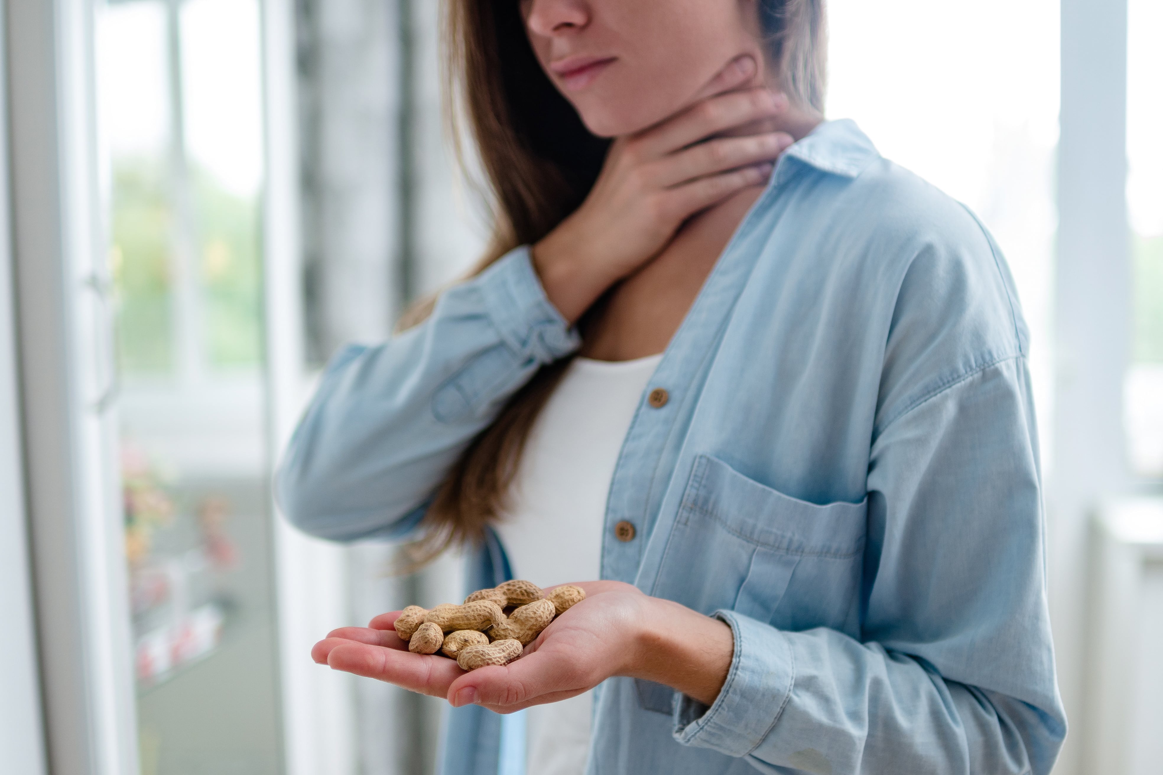 Person holding peanuts in one hand while touching the neck with the other, indicating a possible allergic reaction.