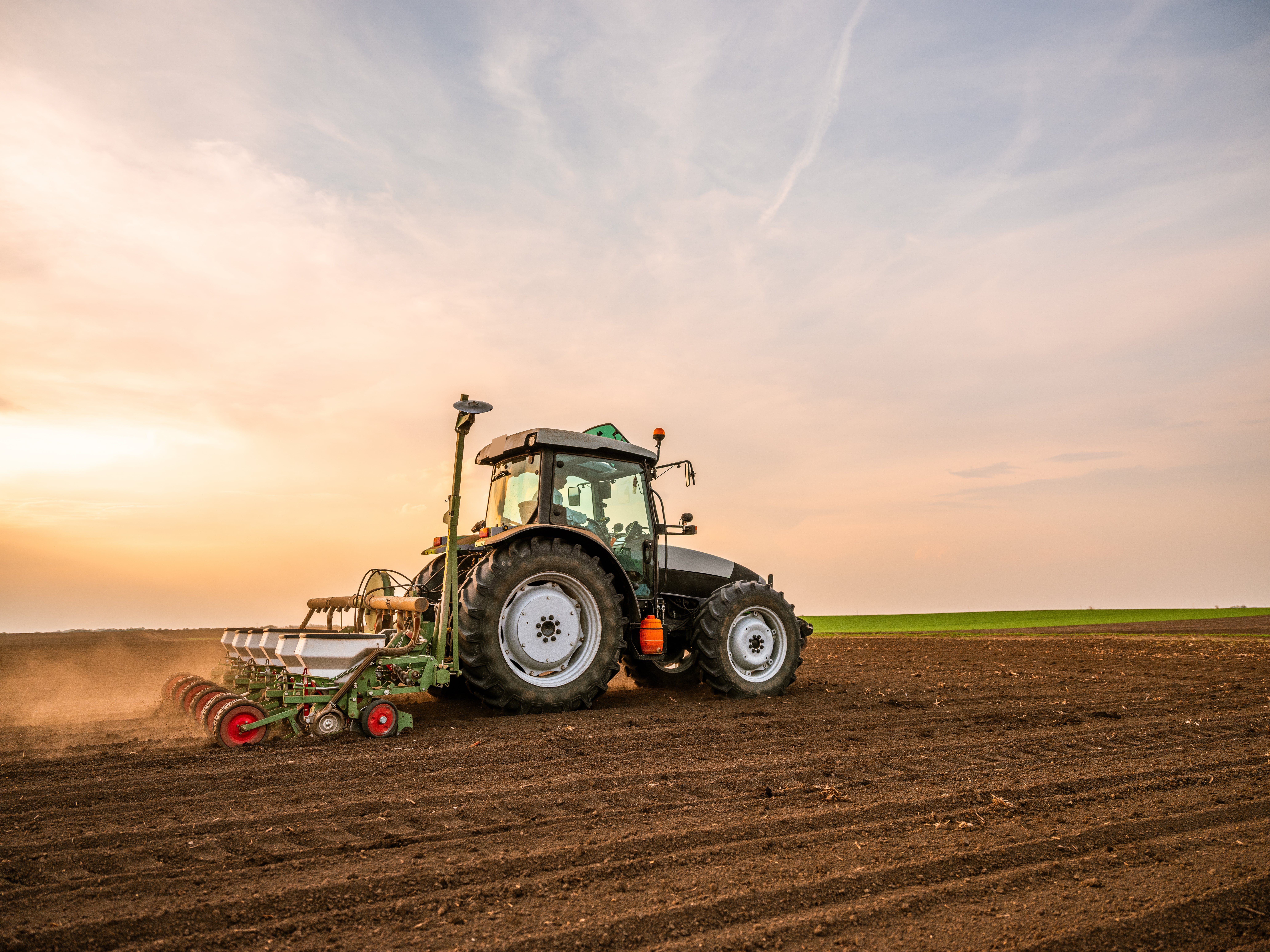Agricultural tractor working on a large field at sunset, preparing the soil for planting under a partly cloudy sky.