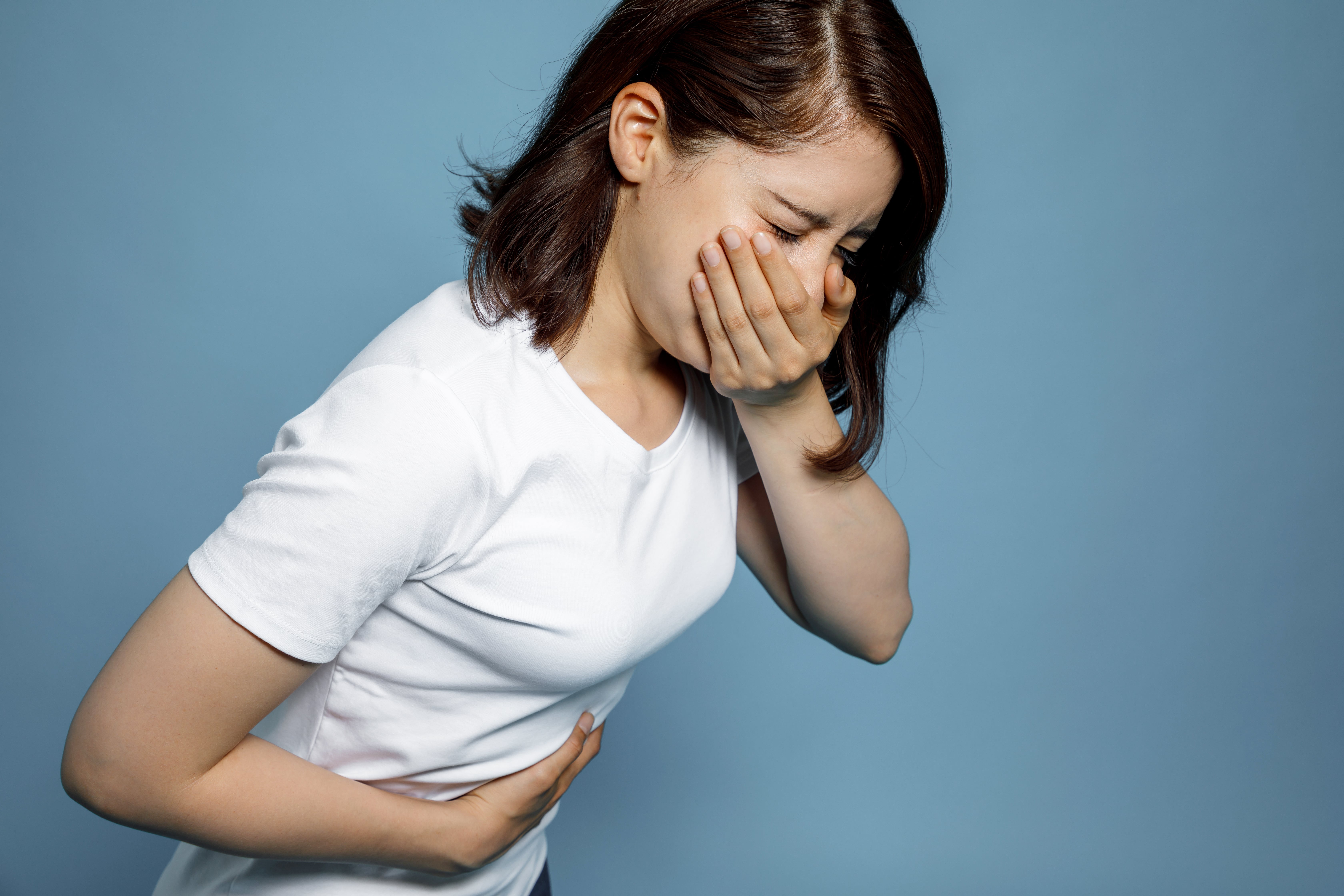 Person wearing a white shirt holding the stomach with one hand and the neck with the other, against a blue background.
