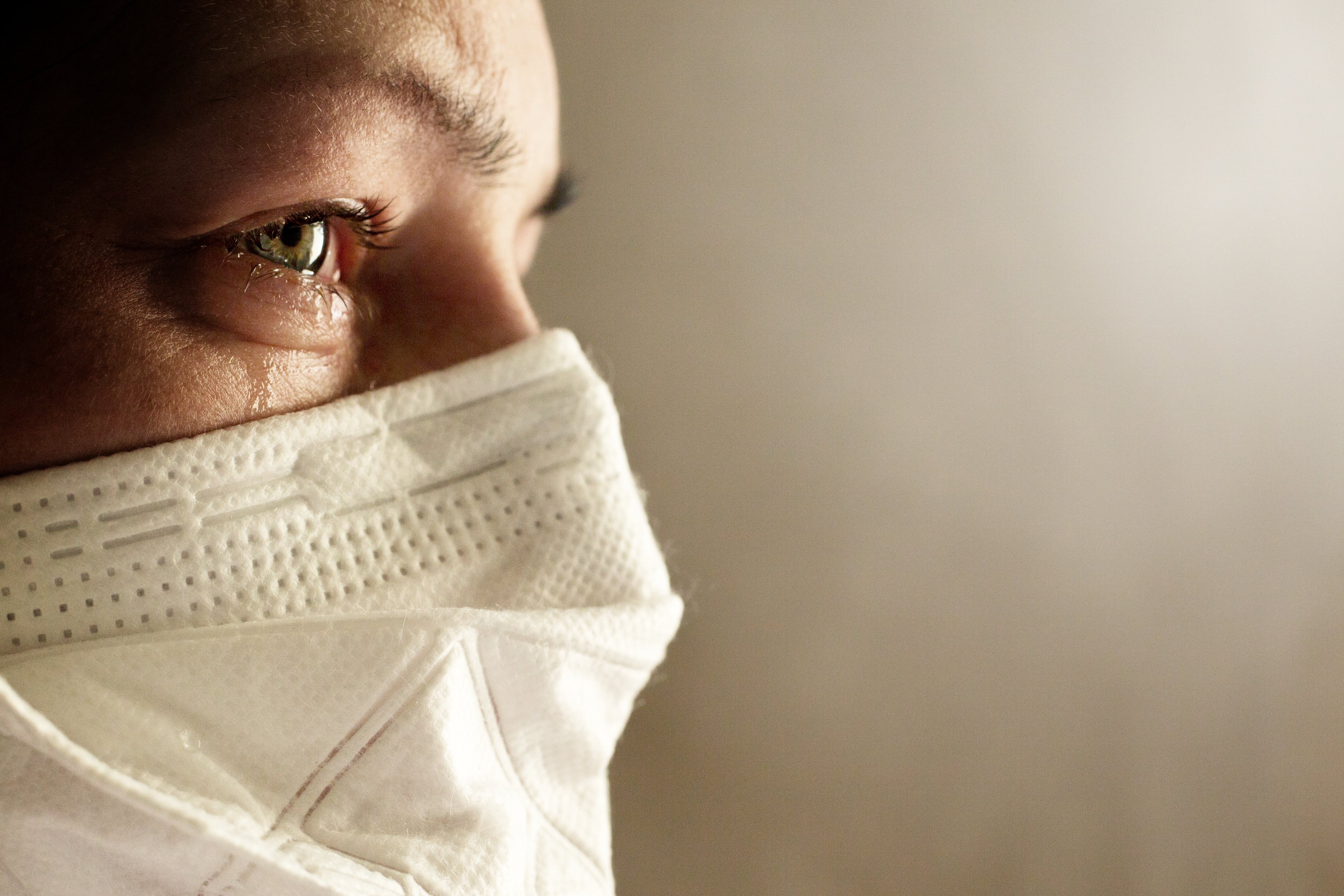 Person wearing an orange sweater adjusting the straps of a blue surgical face mask.