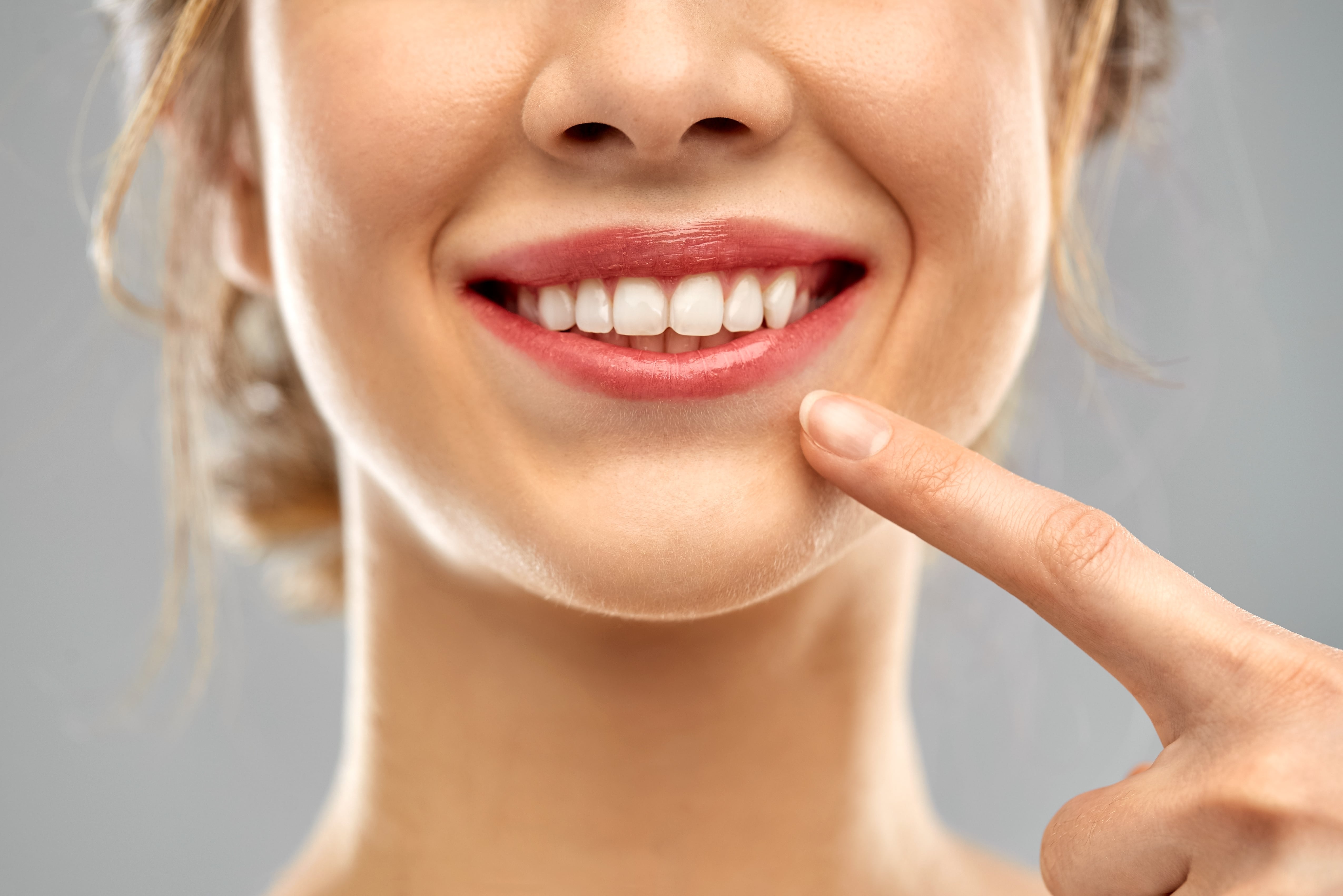 Close-up of a person smiling with white teeth, pointing to their mouth with an index finger.
