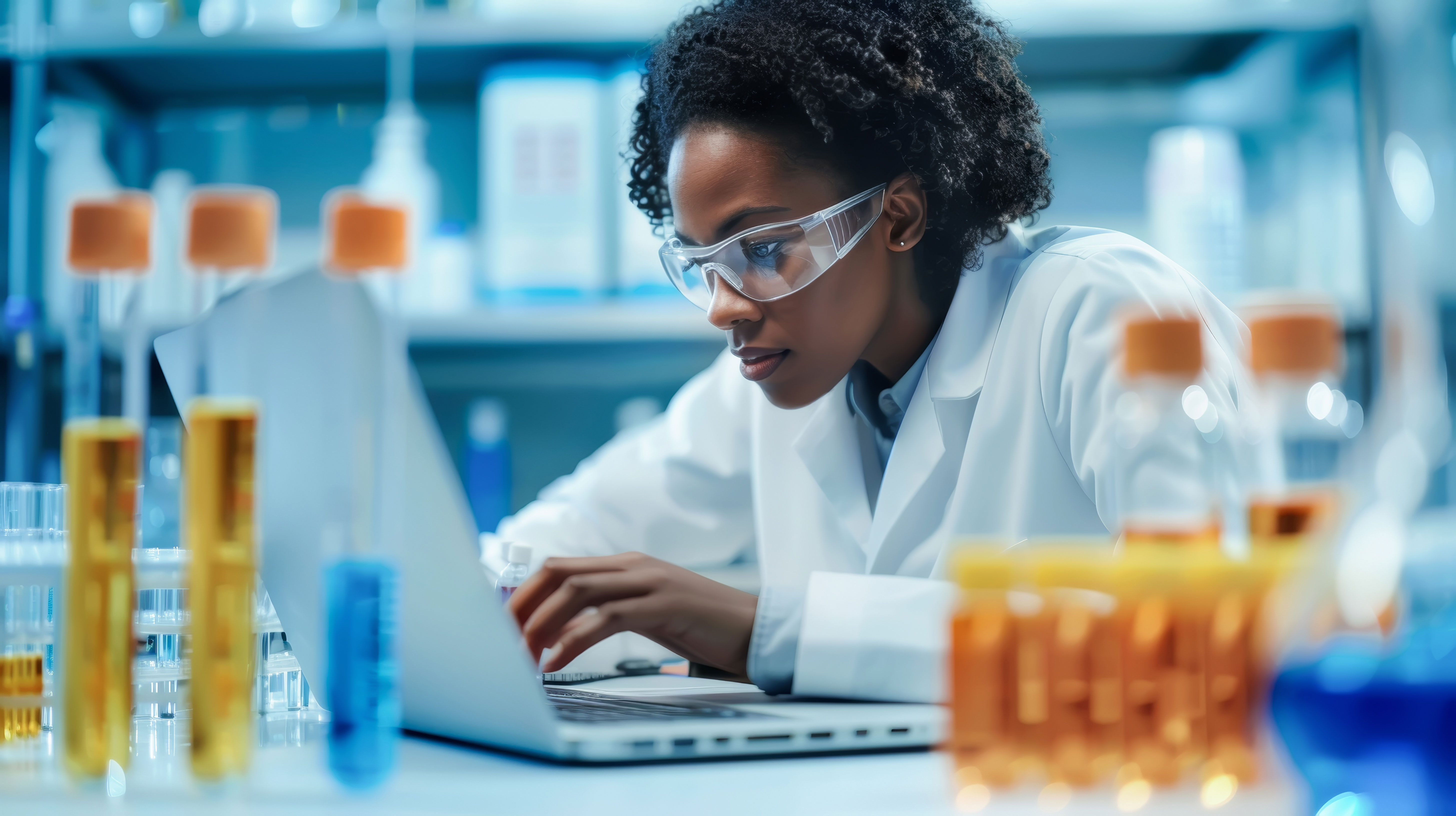 Scientist working with samples and chemicals while using a laptop in the laboratory
