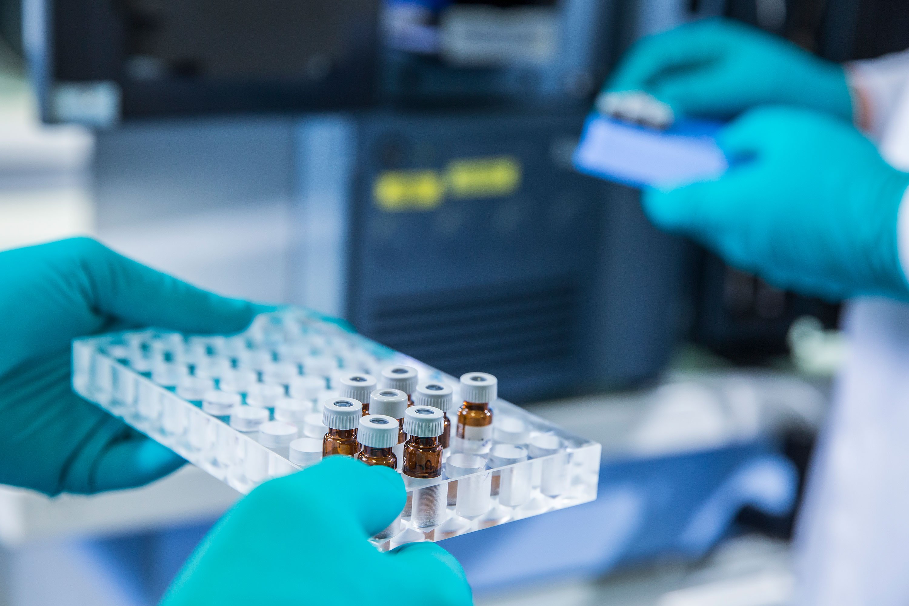 Two gloved hands are handling transparent trays filled with small vials