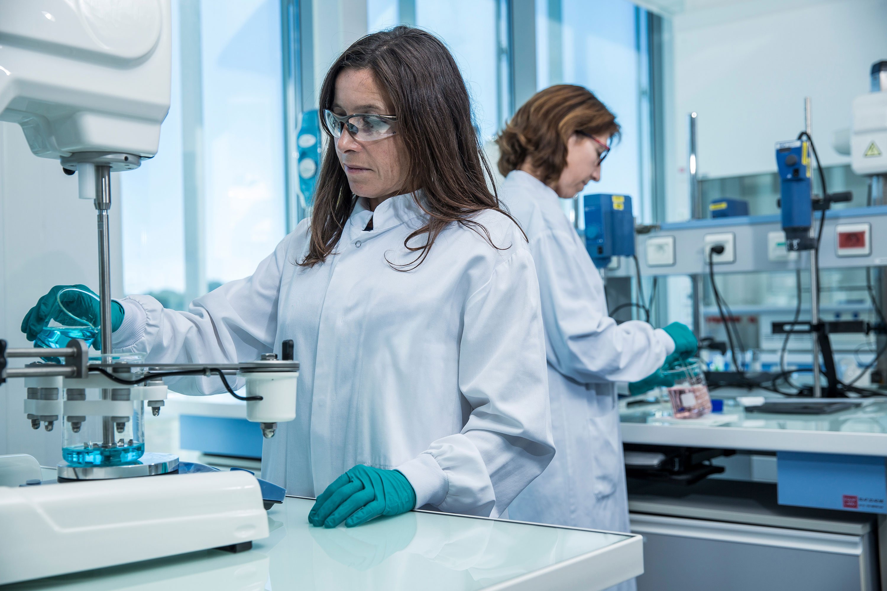Two female scientists standing in front of a stirring equipment on a bench