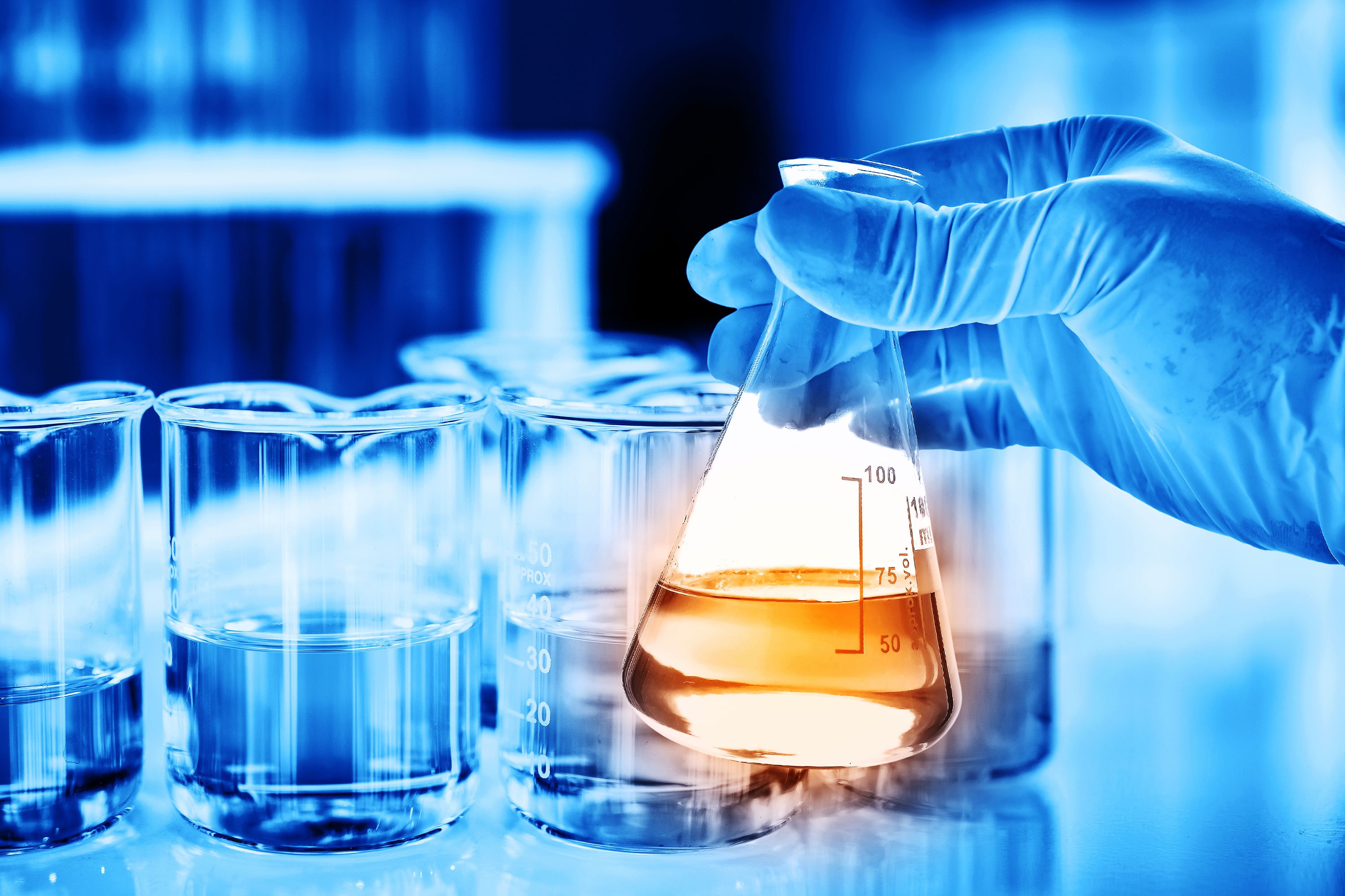 A hand, with blue gloves, is handling a flask with orange liquid, on a blue environment