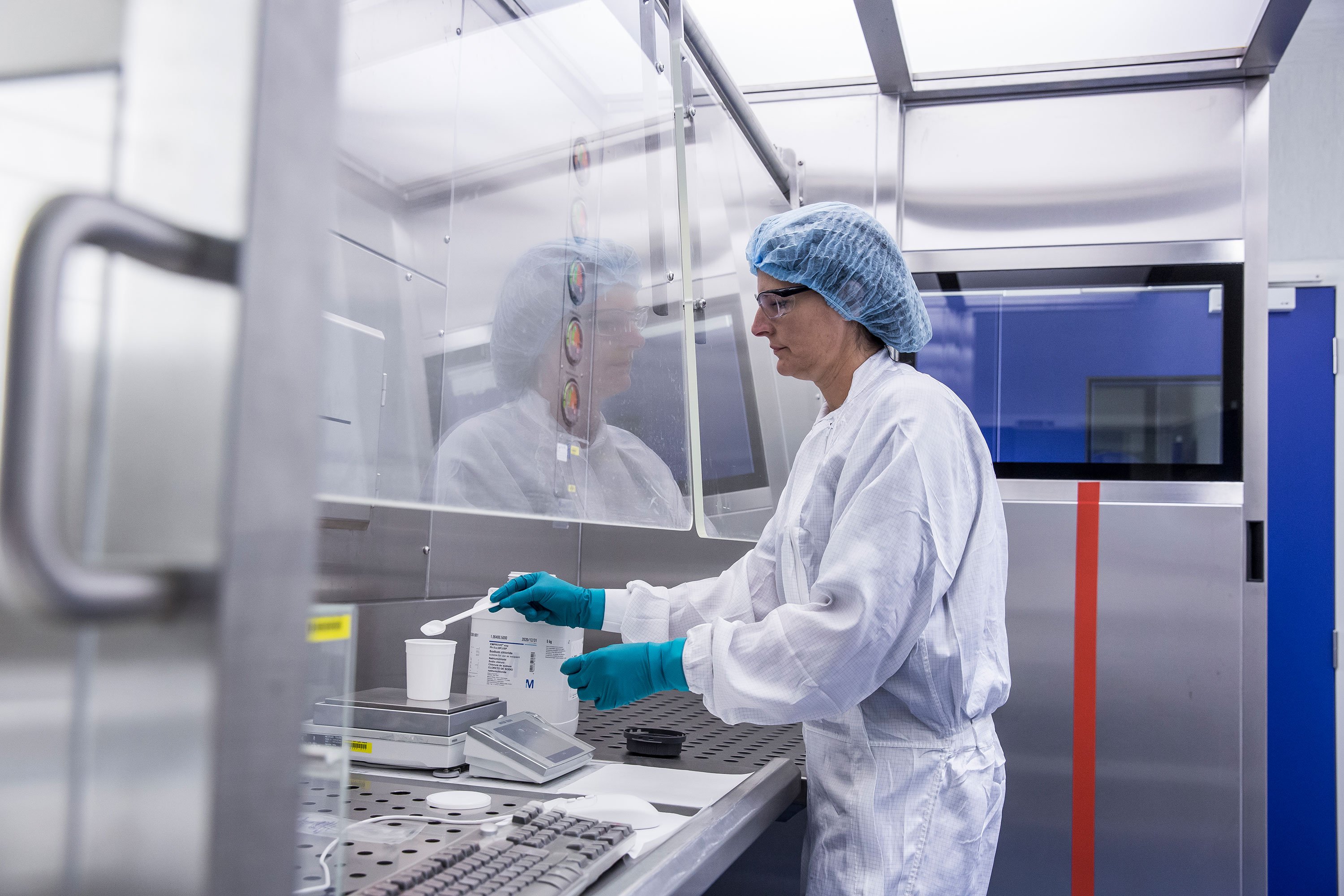 A scientist wearing a labcoat is weighing raw materials under a laminar flow hood