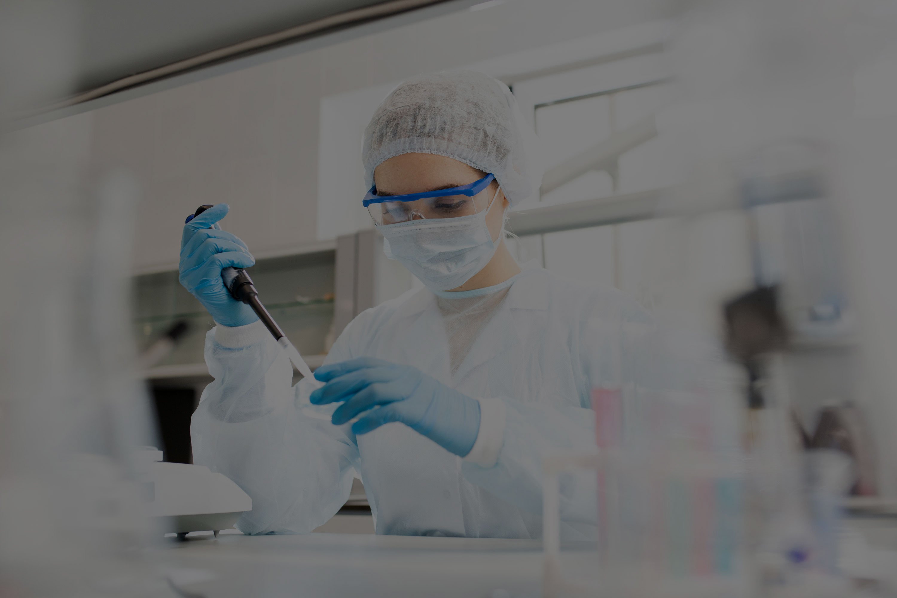 Microbiologist in sterile clothing and safety goggles adding reagent to a petri dish in a laboratory