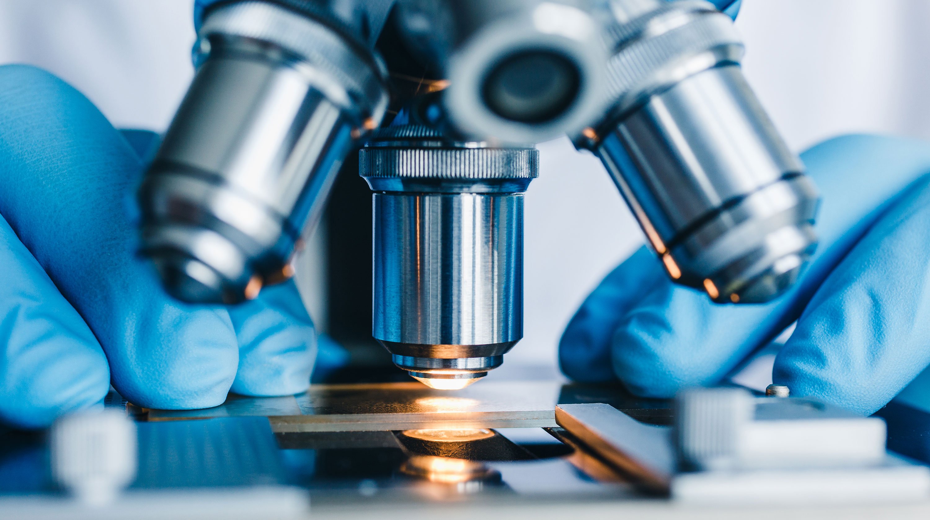 Scientist's gloved hands working with a microscope