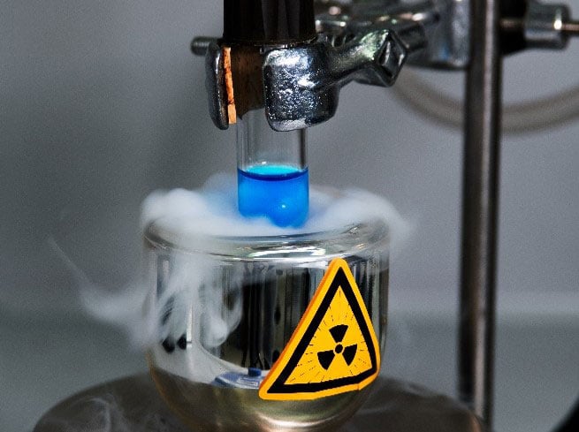 Lab vial with glowing liquid submerged in liquid nitrogen, featuring a prominent radioactivity symbol on its surface. 