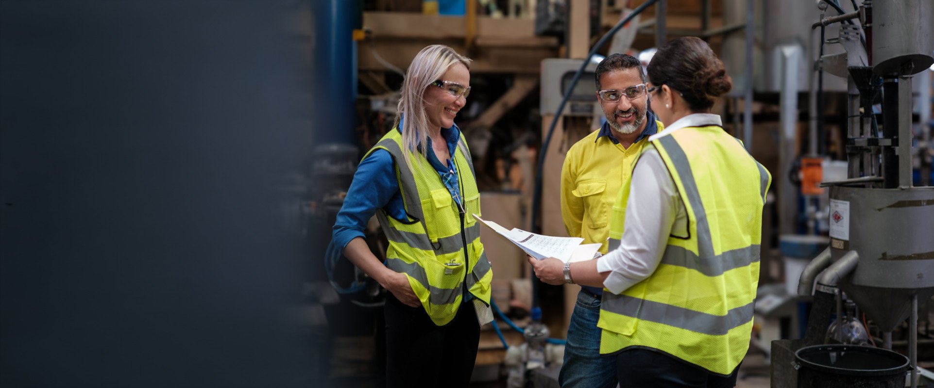 Workers in safety vests reviewing documents in an industrial facility