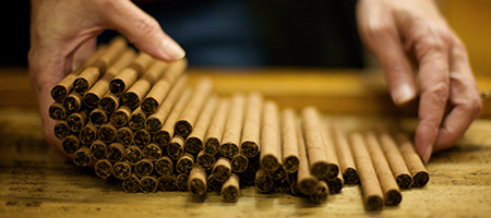 detail of hands laying out large machine-made cigars