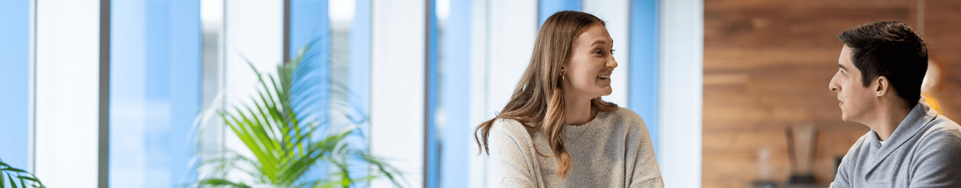 Colleagues engage in conversation across a table in a bright, collaborative office environment.