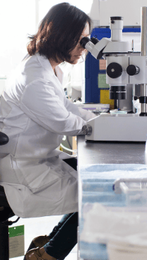 Scientist uses a microscope in a laboratory surrounded by testing supplies and scientific equipment.