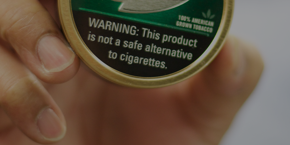 hand holding a can of tobacco with warning label
