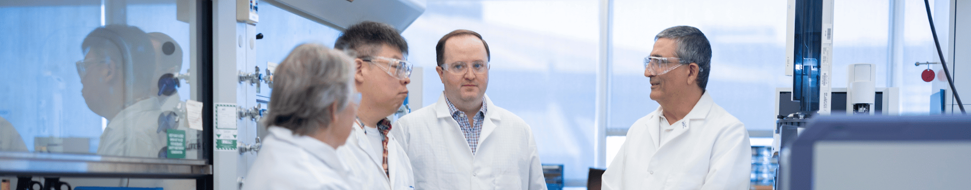 four men standing in a lab discussing business