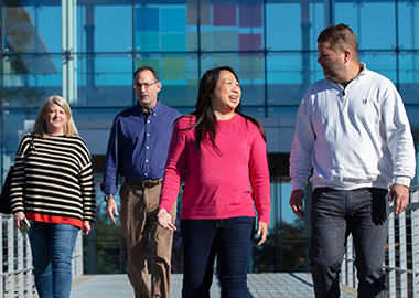 Benefits image - Multi-racial group walking away from a building in male/female pairs.  The Altria mosaic is seen in the background on the building behind glass.