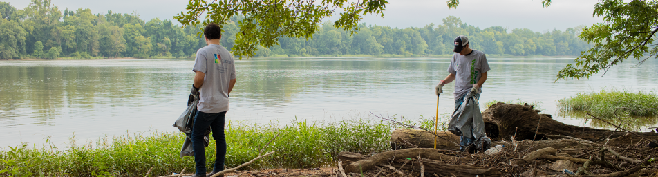 Two male Altria employee volunteering cleaning up beside a James river.