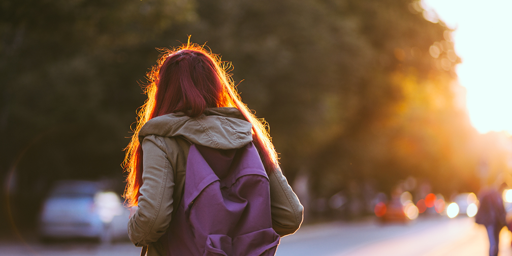 anterior shot of girl with backpack looking at cars at sunset