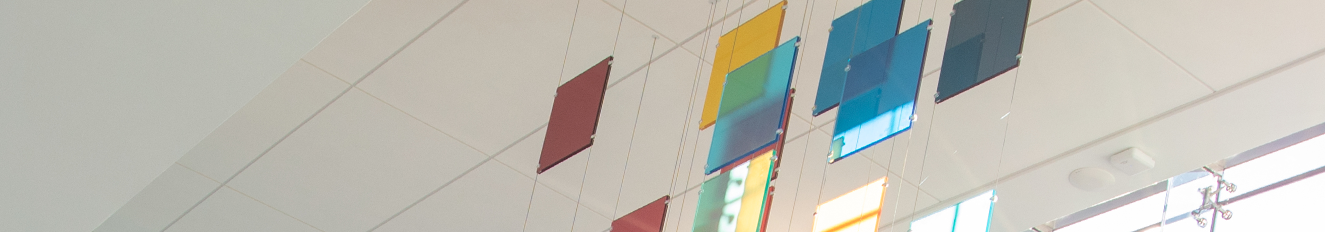 Close up of the deconstructed Altria mosaic, created from multiple squares of glass in the colors of the company logo, each hanging individually via two wires from an off-white ceiling. Light shines through some of the glass panes from high windows on the outside wall. Artwork hangs in the second lobby at the Altria headquarters.