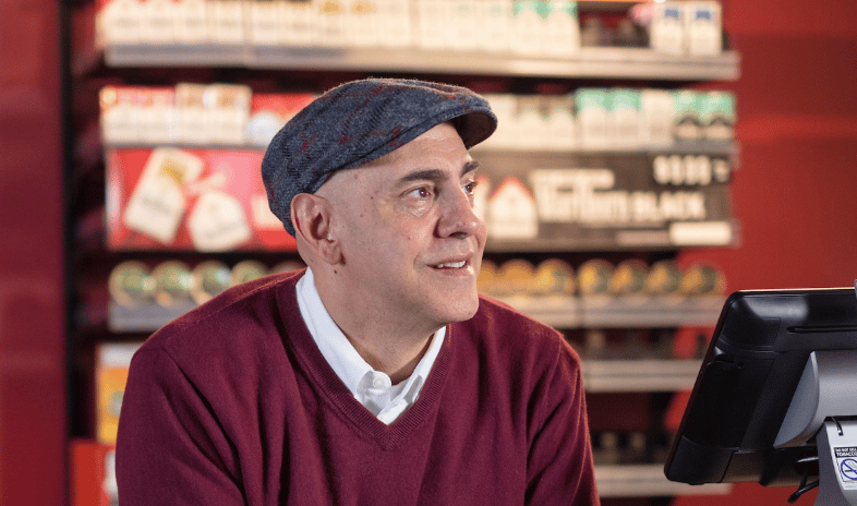male store clerk leaning on counter with we card sign