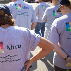 backs of a group of employee volunteers all wearing the same navy blue bill caps and grey short-sleeved volunteer t-shirt with the Altria logo on the back
