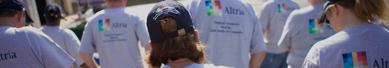 Backs of a group of employee volunteers all wearing the same navy blue bill caps and grey short-sleeved volunteer t-shirt with the Altria logo on the back