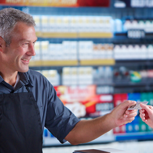 close-up of a white male retailer returning a driver’s id to the customer in a convenience store