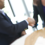 Muted image of a man in a suit and tie shaking hands with a woman in a dark dress at a table